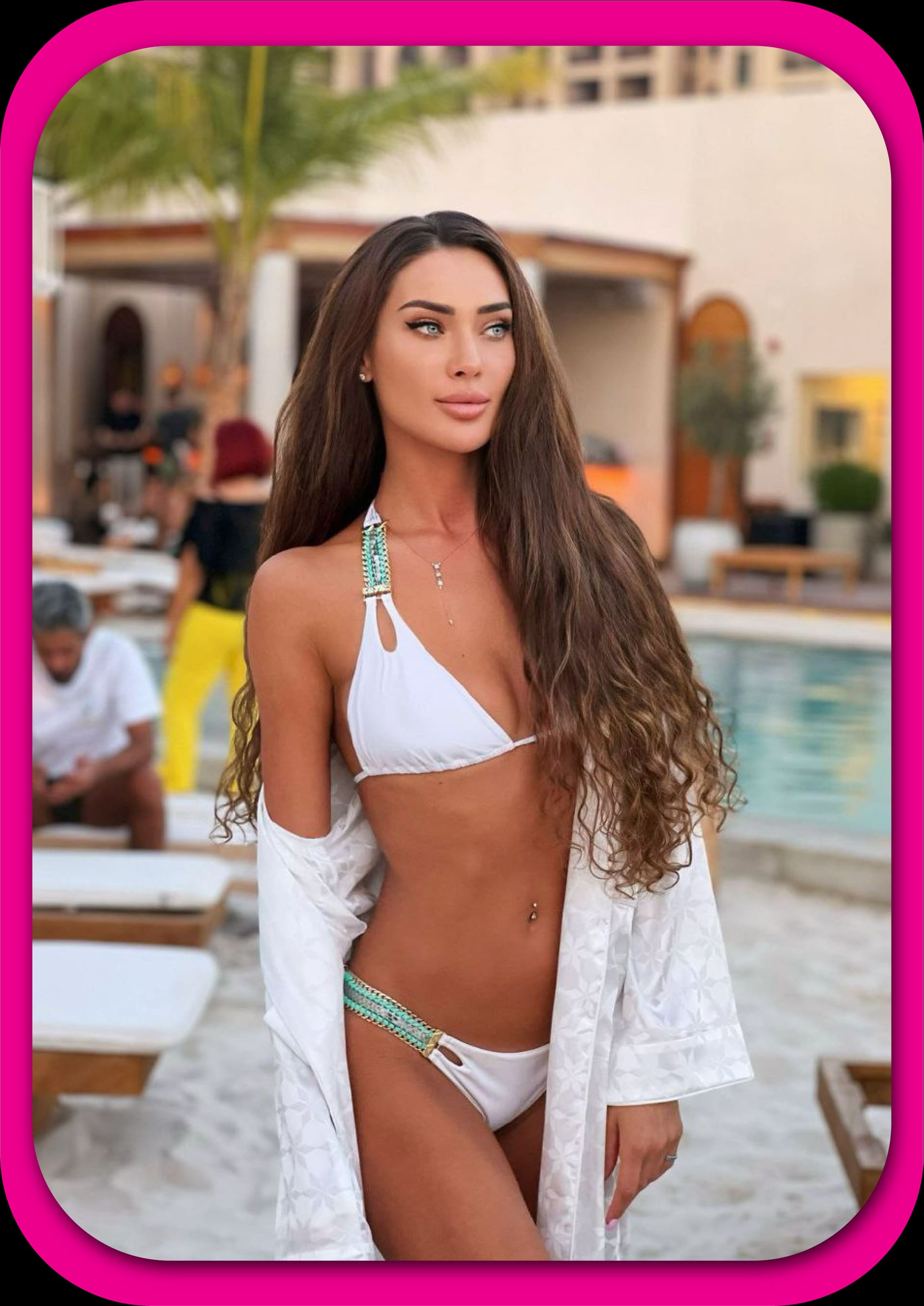 Woman in a white bikini with turquoise straps and a patterned cover-up stands by a pool with lounge chairs.